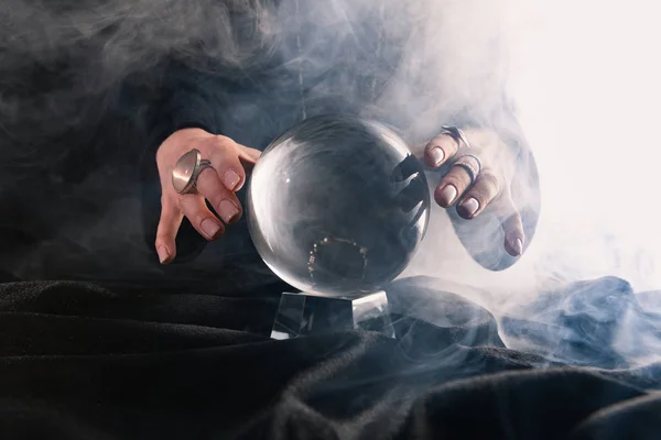 Vue partielle des mains féminines près de la boule de cristal sur fond sombre — Photo de stock