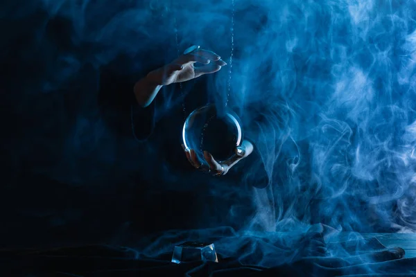 Vista recortada de bruja con bola de cristal sobre fondo azul oscuro - foto de stock