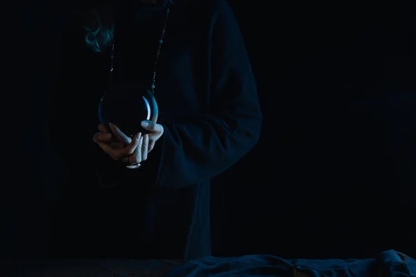 Vista cortada de bruxa com as mãos apertadas segurando bola de cristal no fundo preto — Fotografia de Stock