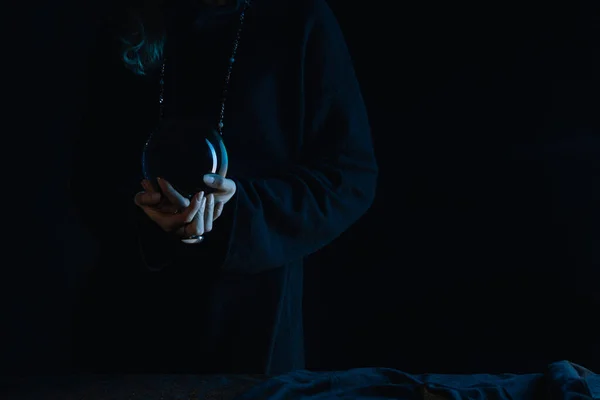 Cropped view of witch with clenched hands holding crystal ball on black background — Stock Photo