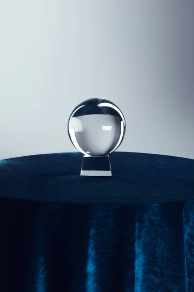Bola de cristal na mesa redonda com toalha de mesa azul escuro no fundo cinza — Fotografia de Stock