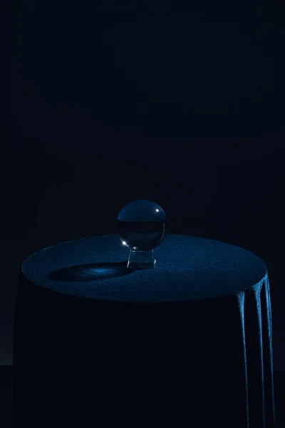 Bola de cristal sobre mesa redonda con mantel azul oscuro sobre fondo negro - foto de stock