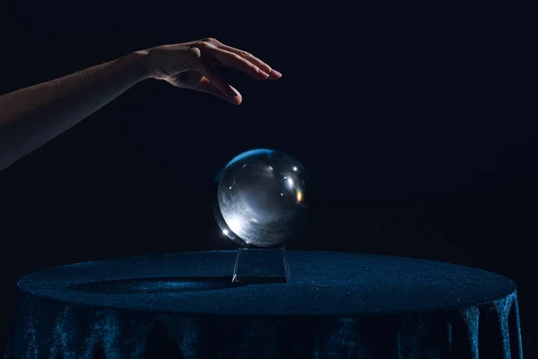 Vista ritagliata della mano femminile sopra la sfera di cristallo sul tavolo isolato su nero — Foto stock