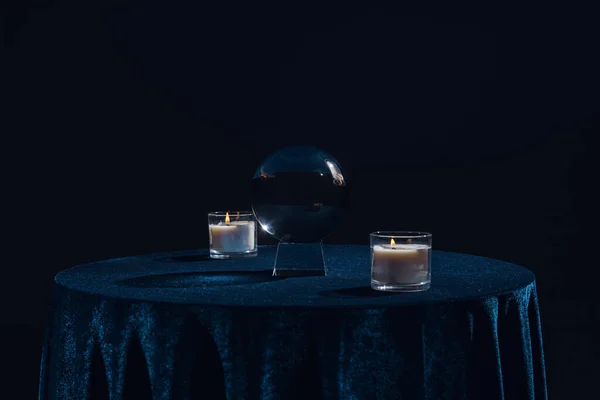 Crystal ball with candles on table isolated on black — Stock Photo