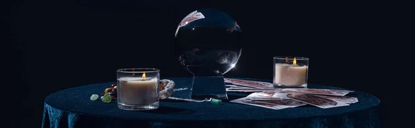 QUIIV, UCRÂNIA - JANEIRO 9, 2020: bola de cristal com velas, cartas de tarô, pedras e corrente na mesa redonda isolada em preto, tiro panorâmico — Fotografia de Stock