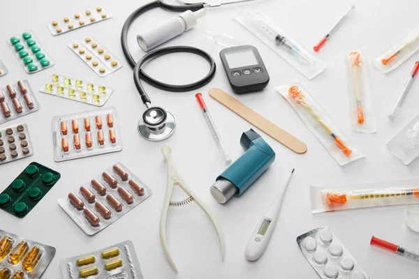 Visão de alto ângulo de medicamentos, estetoscópio, termômetro e objetos médicos em branco — Fotografia de Stock