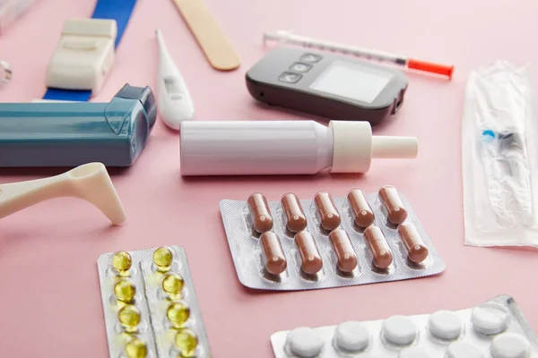 Enfoque selectivo de cápsulas, pastillas y objetos médicos sobre fondo rosa - foto de stock