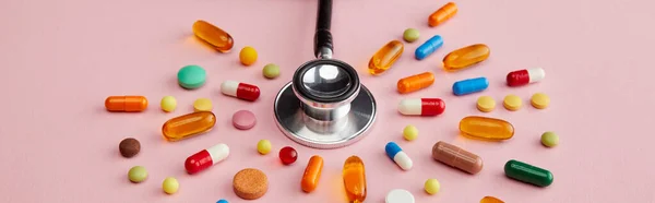 High angle view of stethoscope near bright colorful pills on pink background, panoramic shot — Stock Photo