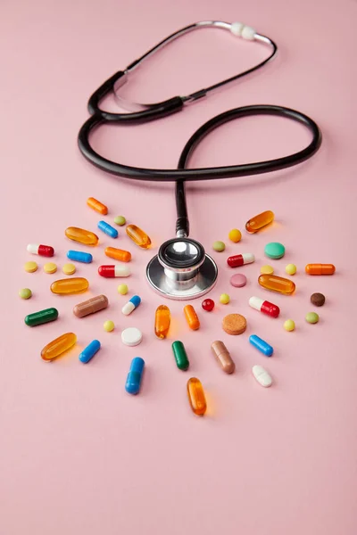 High angle view of stethoscope near bright colorful pills on pink background — Stock Photo