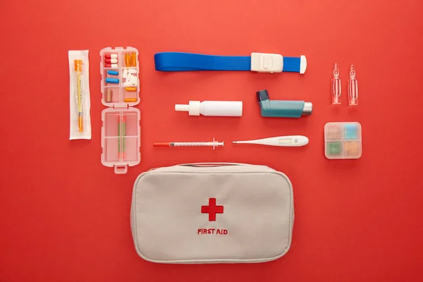 Flat lay with first aid kit, pills and medical objects on red background — Stock Photo