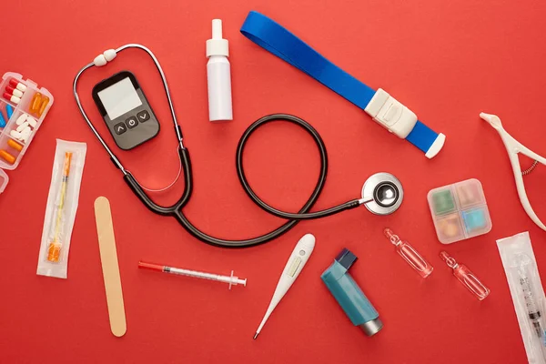 Vue du dessus du stéthoscope, de l'inhalateur d'asthme, des médicaments et des objets médicaux sur fond rouge — Photo de stock