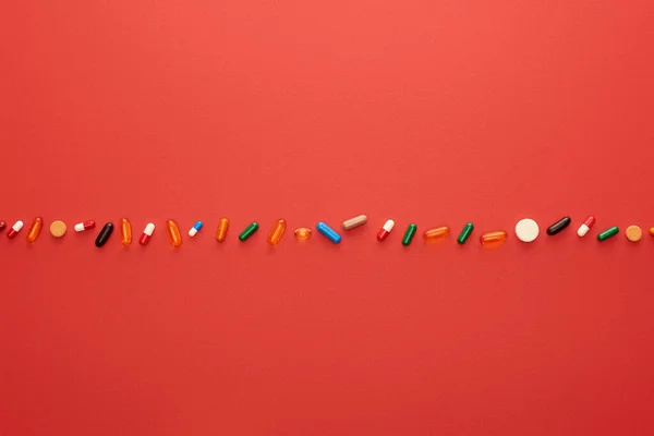 Vista dall'alto di colorate pillole luminose su sfondo rosso — Stock Photo