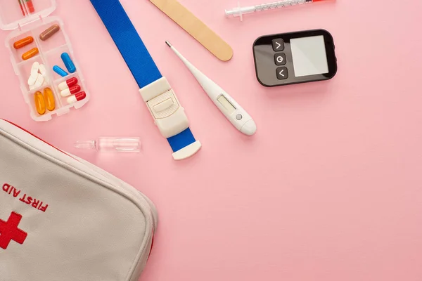 Вид сверху аптечки, таблеток и медицинских предметов на розовом фоне — стоковое фото