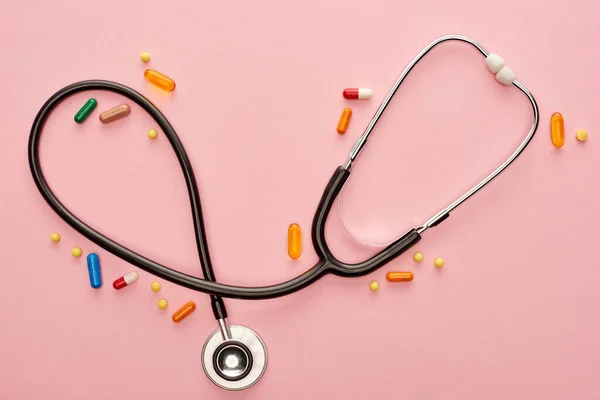 Vue du dessus des pilules colorées avec stéthoscope sur fond rose — Photo de stock