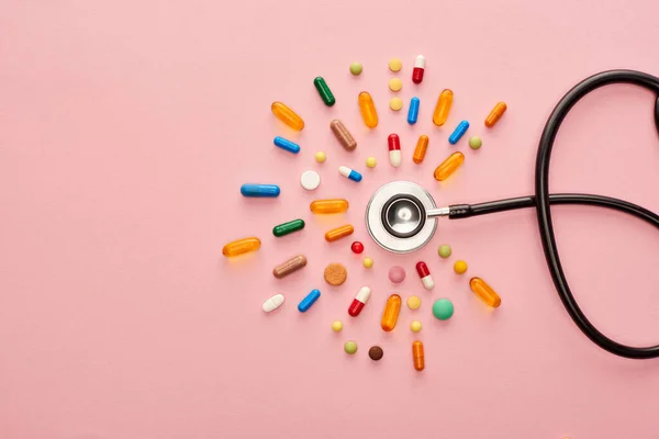 Vue du dessus des pilules colorées et stéthoscope sur fond rose — Photo de stock