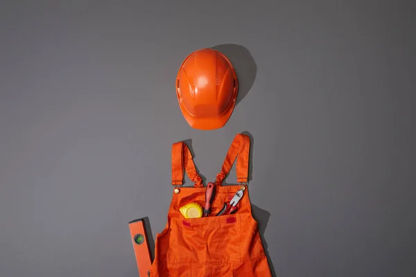 Top view of orange helmet and overalls with measuring tape, screwdriver and pliers on grey background — Stock Photo