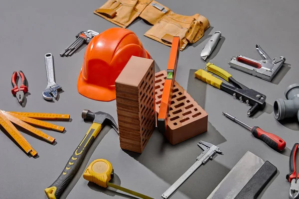 High angle view of helmet, bricks and industrial tools on grey background — Stock Photo