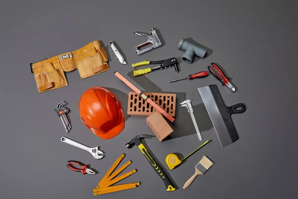 Vista superior de tijolos, cinto de ferramentas, capacete e ferramentas industriais em fundo cinza — Fotografia de Stock