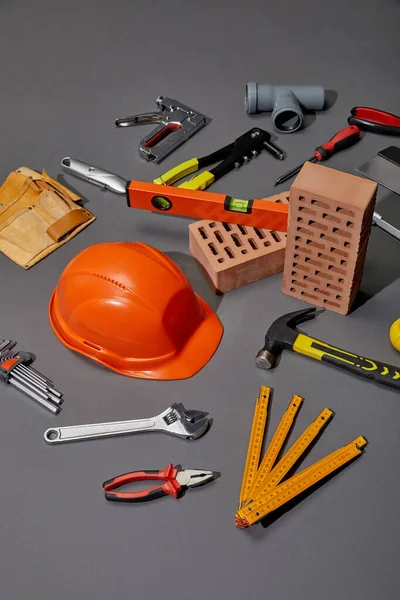 High angle view of tool belt, bricks, industrial tools and orange helmet on grey background — Stock Photo