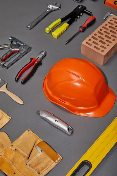 Flache Verlegung mit orangefarbenem Helm, Werkzeuggürtel, Ziegel, Industriewerkzeug und Pinsel auf grauem Hintergrund — Stockfoto