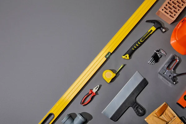 Tendido plano con ladrillo, martillo, cinta métrica, casco, correa de herramientas y herramientas industriales sobre fondo gris - foto de stock