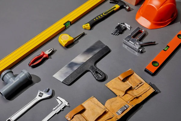 Tendido plano con casco, correa de herramientas y herramientas industriales sobre fondo gris - foto de stock