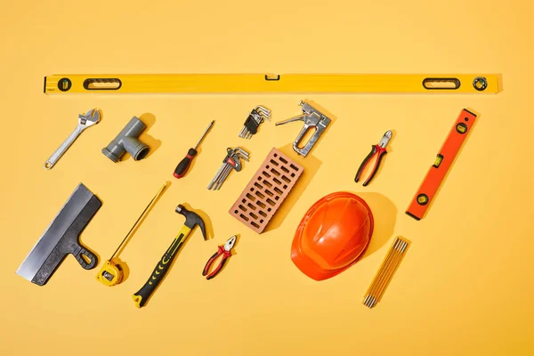 Tendido plano con herramientas industriales, casco de ladrillo y naranja sobre fondo amarillo - foto de stock