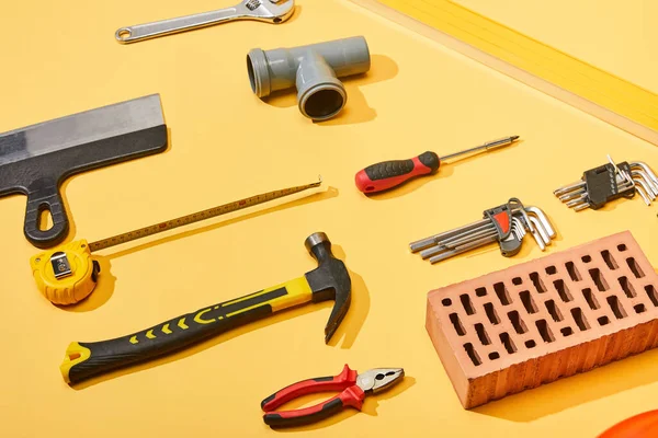 Flat lay with hammer, pipe connector, angle keys, screwdriver, pliers, brick, measuring tape and putty knife on yellow background — Stock Photo