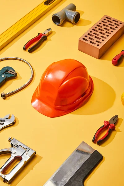 Tendido plano con herramientas industriales, casco y ladrillo, sobre fondo amarillo - foto de stock