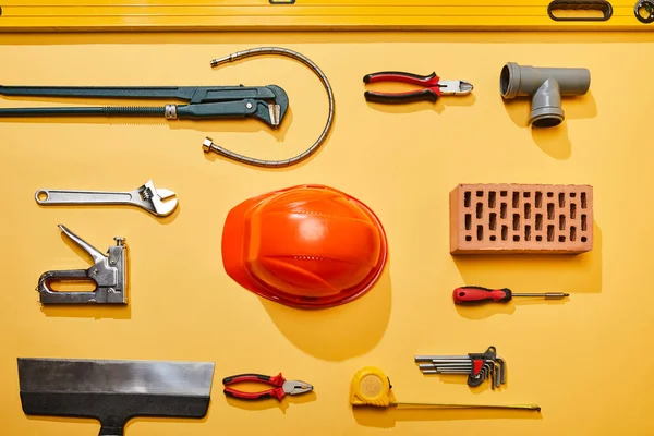 Vista superior de herramientas industriales, casco, manguera de plomería y ladrillo sobre fondo amarillo - foto de stock