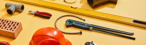 Panoramic shot of spirit level, calipers, plumbing hose, pipe connector, brick, pliers and monkey wrench on yellow background — Stock Photo