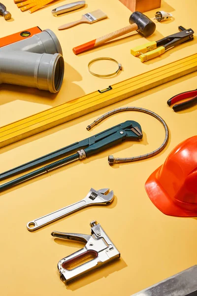 Vue grand angle des outils industriels, tuyau de plomberie, casque et brosse sur fond jaune — Photo de stock