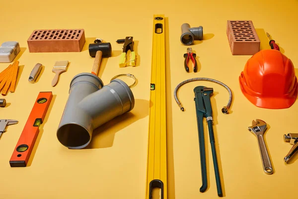 Vista de ángulo alto de herramientas industriales, ladrillos y casco sobre fondo amarillo - foto de stock