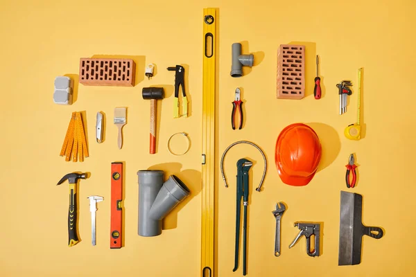 Vista superior de ladrillos, herramientas industriales, casco, manguera de plomería y cinta métrica sobre fondo amarillo — Stock Photo