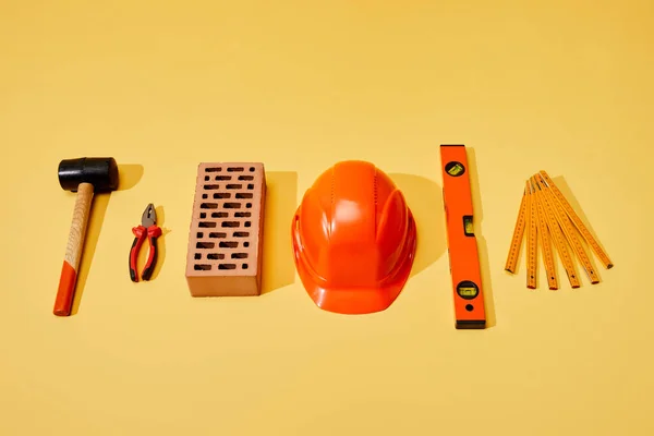 Flat lay with hammer, pliers, brick, helmet, spirit level and folding ruler on yellow background — Stock Photo