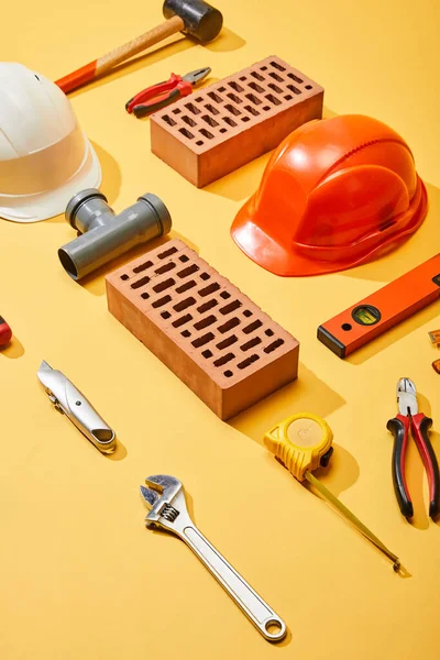 High angle view of bricks, helmets, and industrial tools on yellow background — Stock Photo