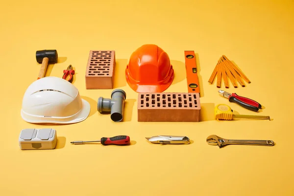 Flache Verlegung mit Ziegeln, Helmen, Industriewerkzeugen und Maßband auf gelbem Hintergrund — Stockfoto