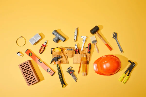 Top view of tool belt, brick, industrial tools and helmet on yellow background — Stock Photo