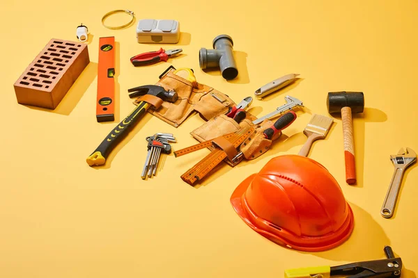 Visão de alto ângulo da correia da ferramenta com ferramentas industriais, tijolo e capacete no fundo amarelo — Fotografia de Stock