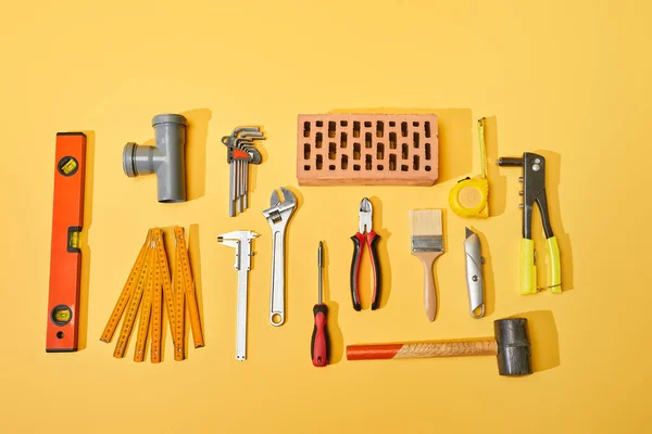 Vista superior de herramientas industriales y ladrillo sobre fondo amarillo - foto de stock