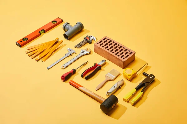 High angle view of industrial tools and brick on yellow background — Stock Photo