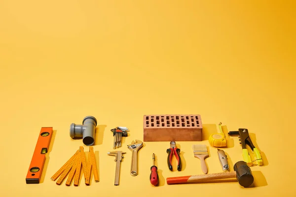 Tendido plano con herramientas industriales y ladrillo sobre fondo amarillo - foto de stock