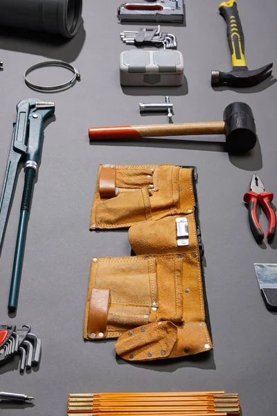 Vista de ángulo alto del cinturón de herramientas, martillos, llave inglesa, cuchillo de masilla, alicates, pinzas, pistola de remache, llaves de ángulo y grapadora sobre fondo gris - foto de stock