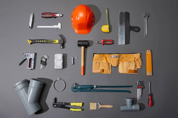 Flat lay of industrial tools, helmet, measuring tape, tool belt and brush on grey background — Stock Photo