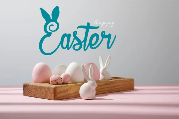 Easter eggs on wooden board with decorative rabbits on pink and grey with happy Easter illustration — Stock Photo