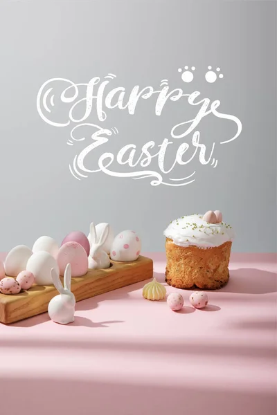 Uova di Pasqua su tavola di legno con conigli decorativi vicino torta pasquale su sfondo rosa e grigio con felice illustrazione pasquale — Foto stock