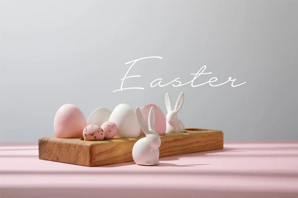 Uova di Pasqua su tavola di legno con conigli decorativi su rosa e grigio con illustrazione pasquale — Foto stock