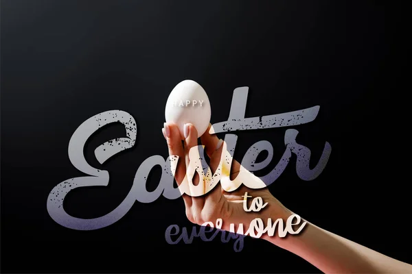 Cropped view of woman holding chicken egg isolated on black with happy Easter to everyone illustration — Stock Photo