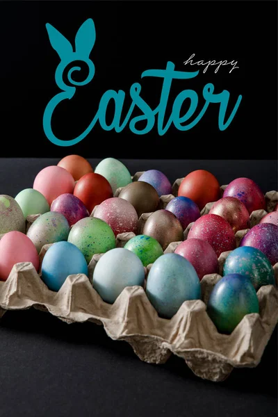 Egg tray with colorful Easter eggs on black background with happy Easter illustration — Stock Photo
