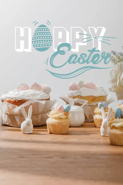 Selektiver Schwerpunkt von Cupcakes mit dekorativen Hasen, Zuckerdose, Osterkuchen und Blumen isoliert auf Grau mit frohen Ostern Illustration — Stockfoto